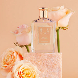 Floris - Bouquet de la Reine klarer Flakon mit goldenem Verschluss umgeben von zarten Pastellrosen auf beigem Hintergrund