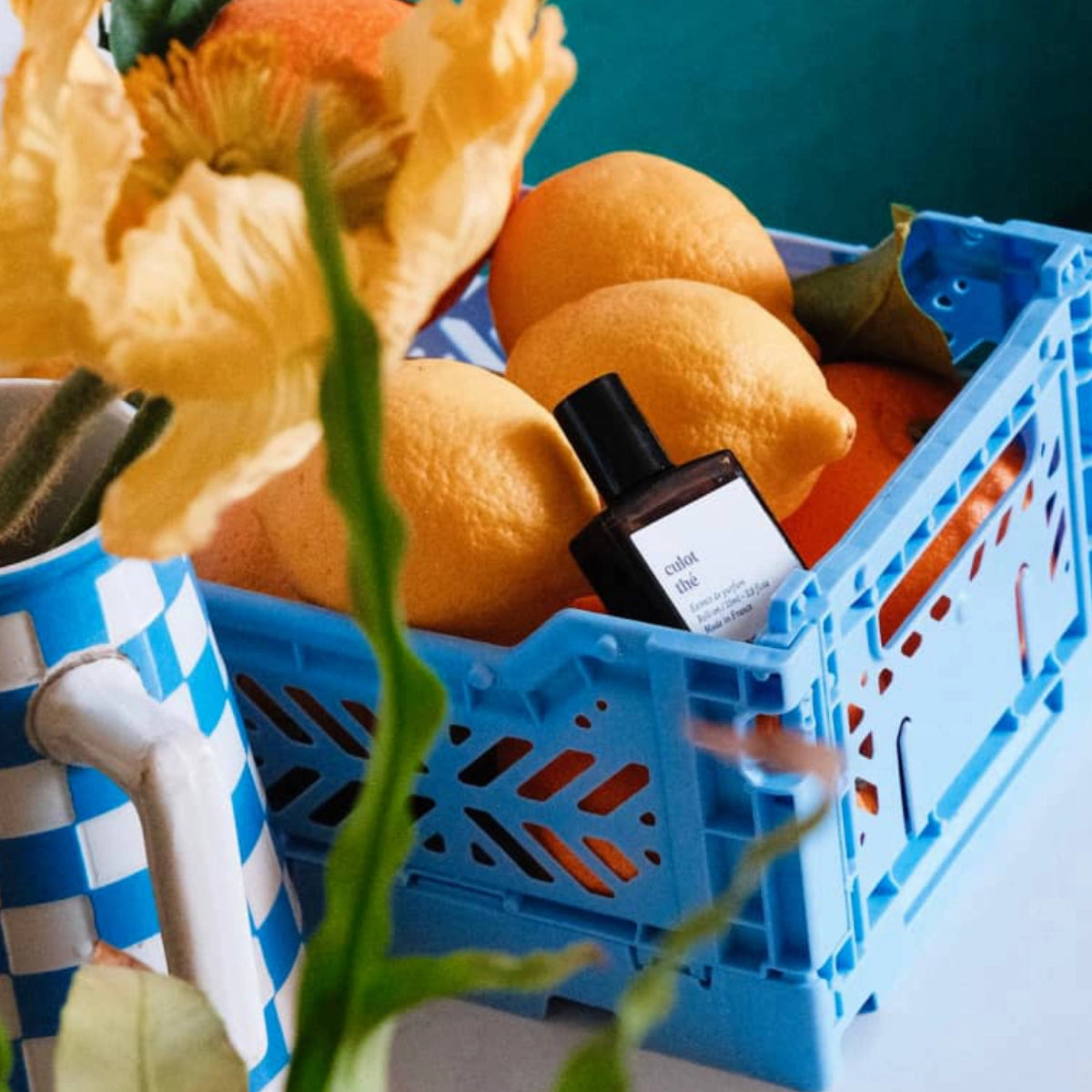 Versatile - Culot Thé Flakon in schwarzer Verpackung zwischen frischen Zitronen in blauer Kiste auf hellem Untergrund