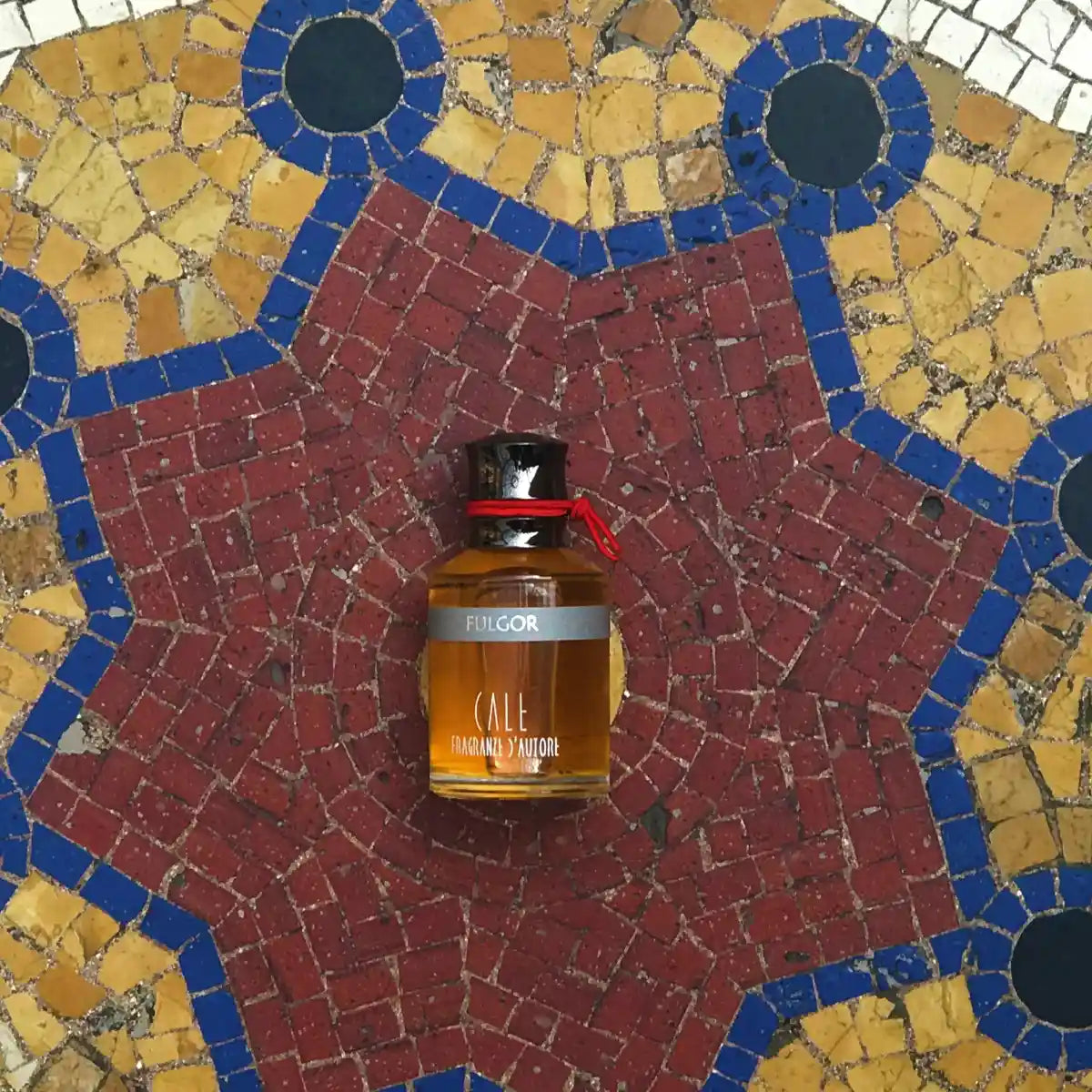 Calé Fragranze d'Autore - Fulgor Parfumflakon mit rotem Band auf farbigem Mosaiksteinfußboden präsentiert