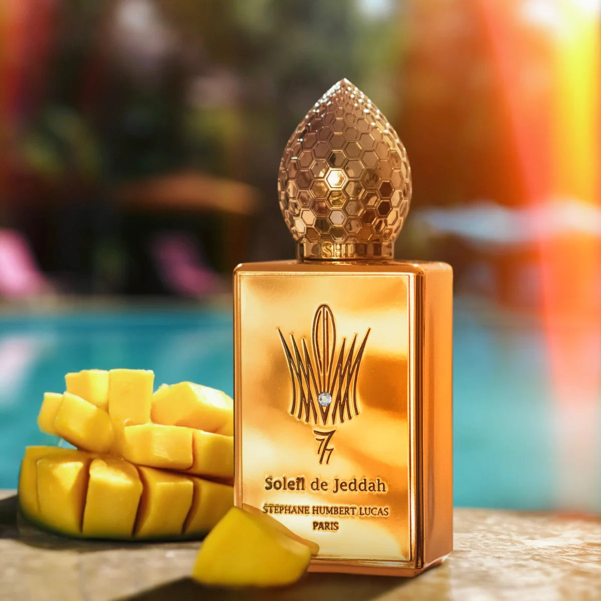 Stéphane Humbert Lucas 777 - Mango Kiss Parfumflakon mit goldglänzendem Design und Mangostücken vor Poolkulisse bei Sonnenuntergang