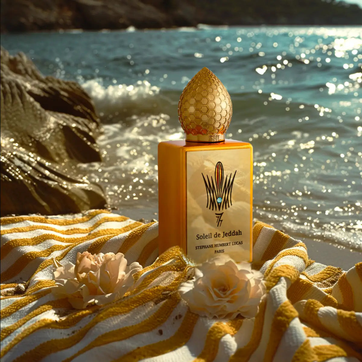 Stéphane Humbert Lucas 777 - Mango Kiss Flakon mit goldgelbem Design am Meer auf gestreiftem Tuch in warmem Licht