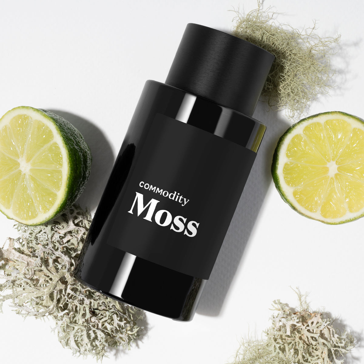 Commodity - Moss Parfumflakon in schwarzem Design liegend mit Limettenscheiben und Moos auf weißem Hintergrund