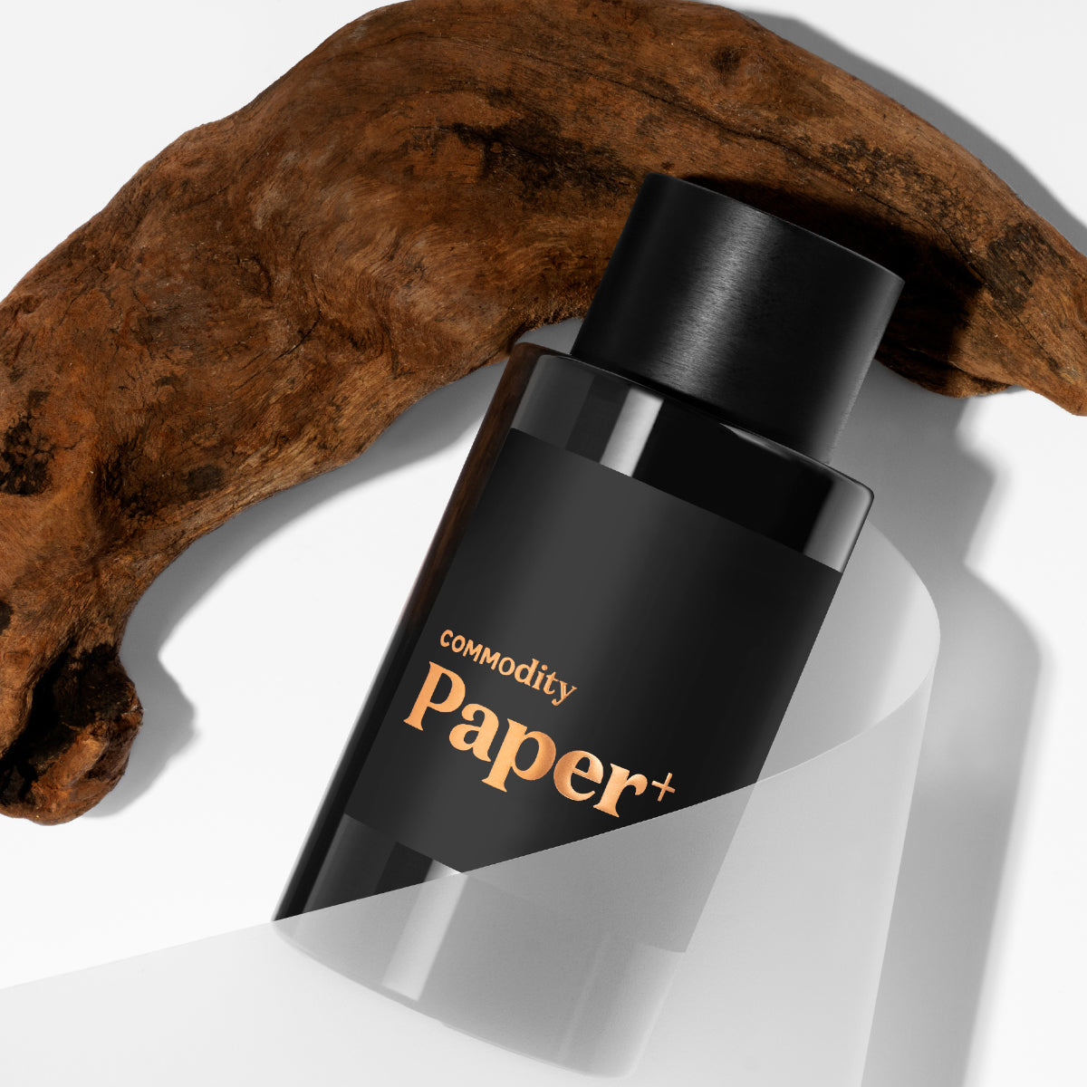 Commodity - Paper+ Flakon mit mattschwarzem Design und kupferfarbenem Schriftzug vor hellgrauem Hintergrund mit Holzdekor