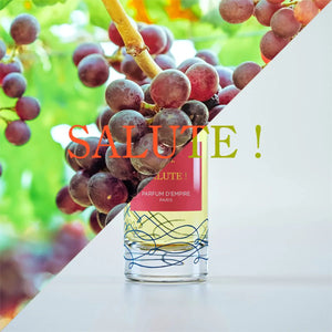 Parfum d'Empire - Salute! Flakon mit rotem Etikett vor Hintergrund mit reifen roten Weintrauben in natürlichem Licht