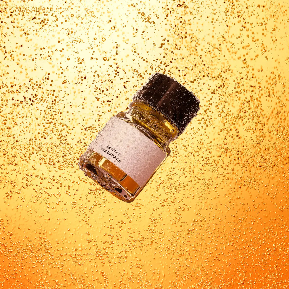Headspace - Santal Flakon mit bernsteinfarbenem Inhalt und schwarzem Deckel vor perlender blasser Orangekulisse