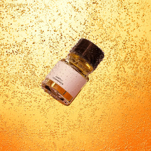Headspace - Santal Flakon mit bernsteinfarbenem Inhalt und schwarzem Deckel vor perlender blasser Orangekulisse