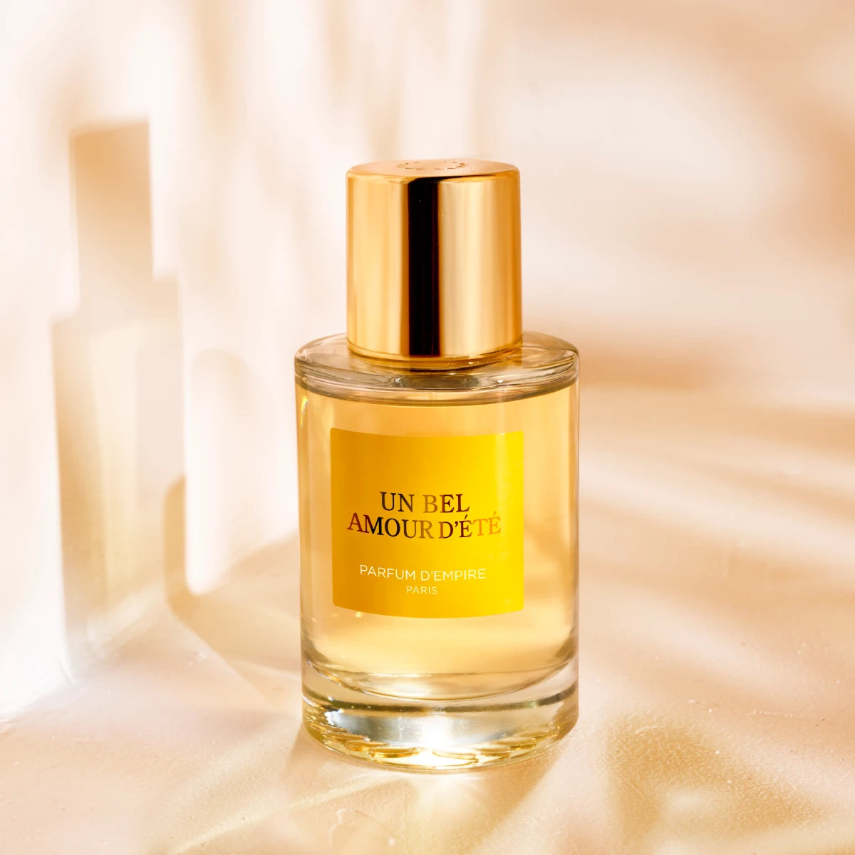 Parfum d'Empire - Un Bel Amour d’Été edler Flakon mit goldfarbenem Verschluss und gelbem Label vor warmem Hintergrund