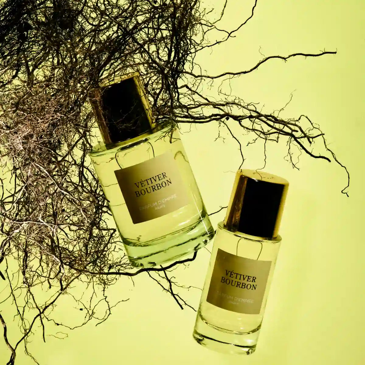 Parfum d'Empire - Vétiver Bourbon Flakons mit goldenem Verschluss vor natürlichen Vetiverwurzeln in warmem Licht