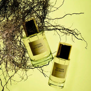 Parfum d'Empire - Vétiver Bourbon Flakons mit goldenem Verschluss vor natürlichen Vetiverwurzeln in warmem Licht
