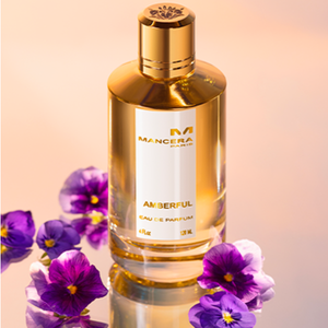 Mancera - Amberful Parfumflakon in goldener Optik umgeben von lila Blüten vor warmem Hintergrund