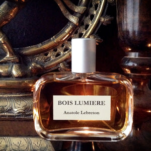 Anatole Lebreton - Bois Lumière Parfumflakon mit bernsteinfarbener Flüssigkeit vor dekorativem Hintergrund