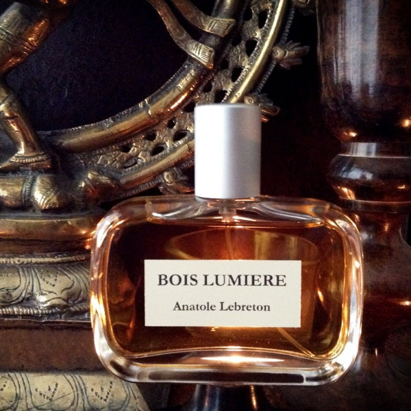 Anatole Lebreton - Bois Lumière Parfumflakon mit bernsteinfarbener Flüssigkeit vor dekorativem Hintergrund