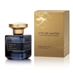 Atelier Materi - Burgundy Oud Parfumflakon in dunklem Glas mit goldenem Deckel neben goldfarbener Verpackung