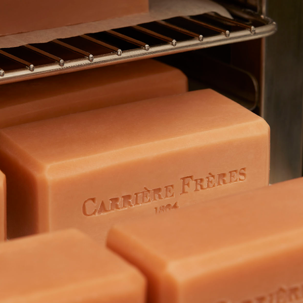 Carrière Frères - Florae - Seife als natürlicher, roséfarbener Block mit geprägtem Logo in warmer Umgebung