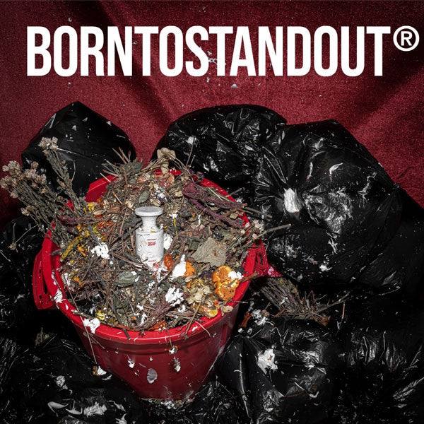 BORNTOSTANDOUT - DGAF Parfumflakon in rotem Eimer mit Trockenblumen und schwarzem Müllsäcken vor rotem Hintergrund