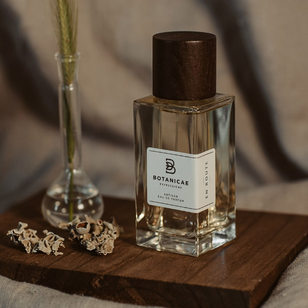 Botanicae - En Route Parfumflakon mit klarem Glas und dunkelbraunem Holzverschluss auf Holzbrett vor warmem Hintergrund