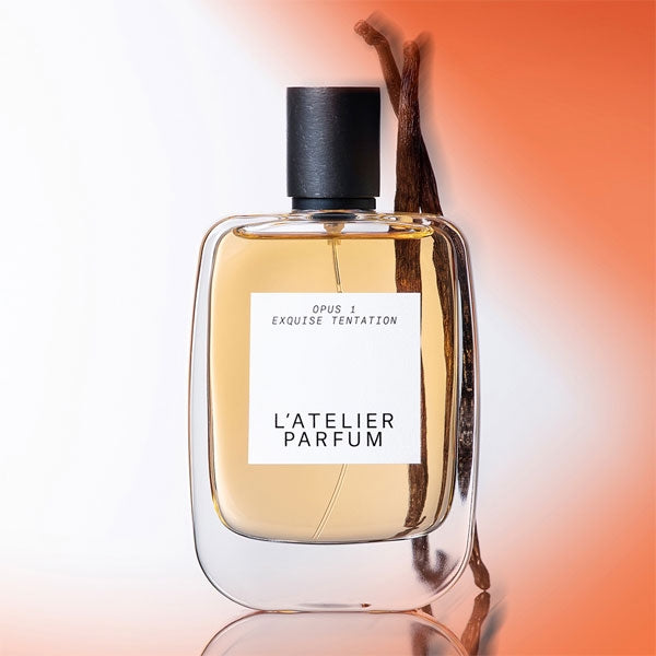 L'Atelier Parfum - Opus 1 - Exquise Tentation Flakon mit Vanilleschoten vor sanft orangefarbenem Hintergrund
