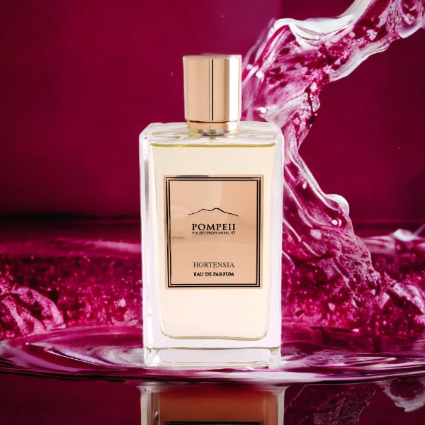 Pompeii - Hortensia Parfumflakon mit klarem Glas und goldenem Etikett vor dynamischem pinkem Wasserhintergrund