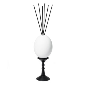 Trudon - L’Œuf Diffusor - Cyrnos mit weißem Ei auf schwarzem Ständer und schwarzen Diffusstäbchen vor weißem Hintergrund