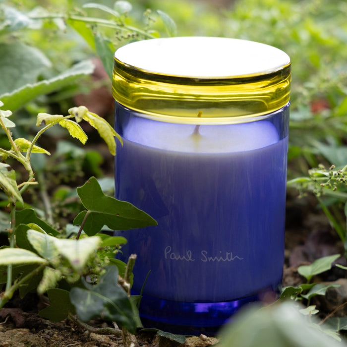 Paul Smith - Leaf - Duftkerze im blauen Glas mit gelbem Rand, umgeben von grüner Pflanzenwelt für frische Duftmomente