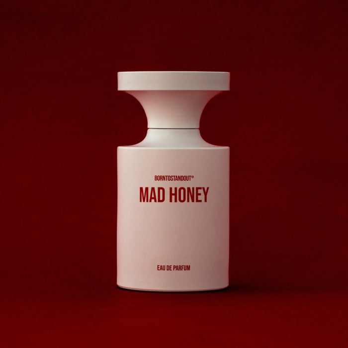 BORNTOSTANDOUT - Mad Honey Parfümflakon in modernem Weiß mit roter Schrift vor tiefrotem Hintergrund