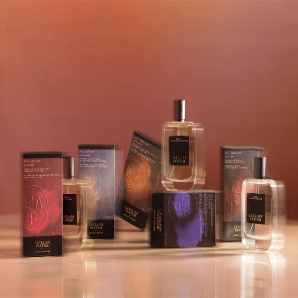 L'Atelier Parfum - Opus 2 - Dose of Rose Flakons mit schwarzen Etiketten und bunten Verpackungen vor warmem Hintergrund