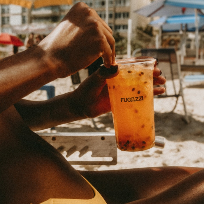 Fugazzi - Passionfroudh zeigt Marke auf durchsichtiger Brause mit Fruchtstücken in sommerlicher Strandumgebung