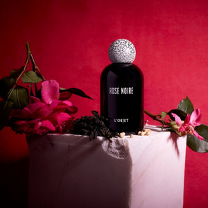 L'Objet - Rose Noire Parfumflakon in schwarzem Glas mit auffälligem weiß-rissigem Verschluss vor rotem Hintergrund