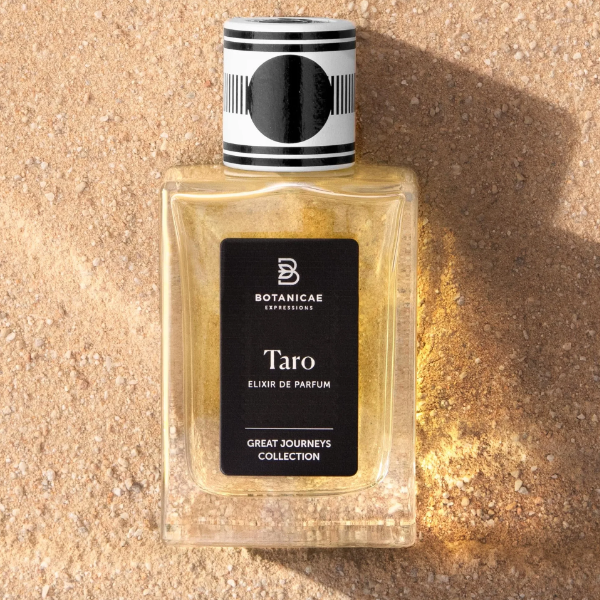 Botanicae - Taro Parfum mit schwarzem Etikett und grafischem Verschluss liegt auf warmem Sand unter Sonnenlicht