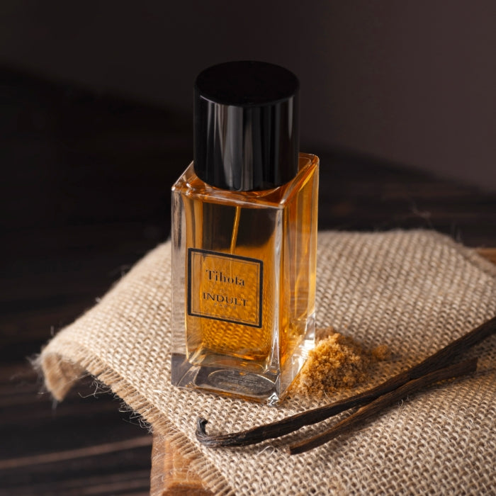 Indult - Tihota Parfum mit bernsteinfarbener Flüssigkeit in klarem Glasflakon und schwarzem Verschluss auf Stoffunterlage